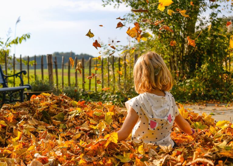 young girl playing in autumn orange leaves outside